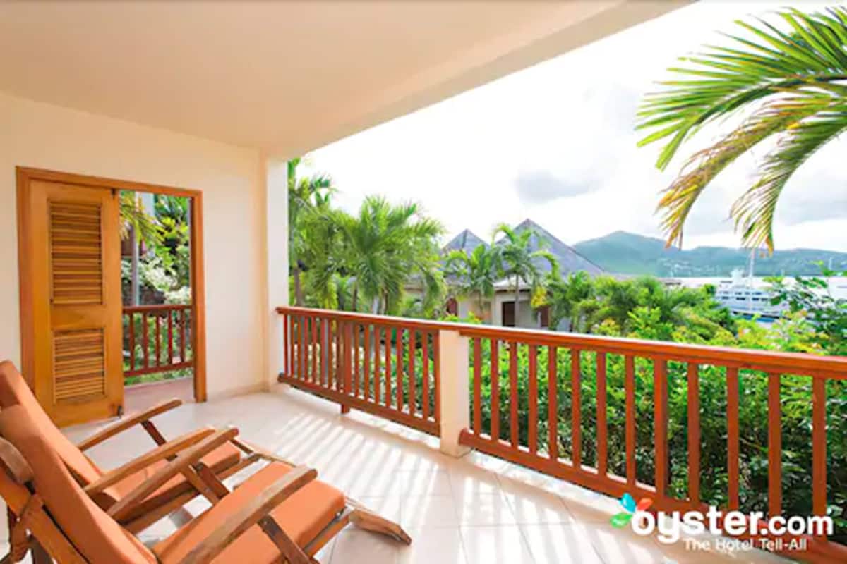 A balcony with wooden railings and lounge chairs, overlooking a lush landscape with palm trees and a mountain in the distance.