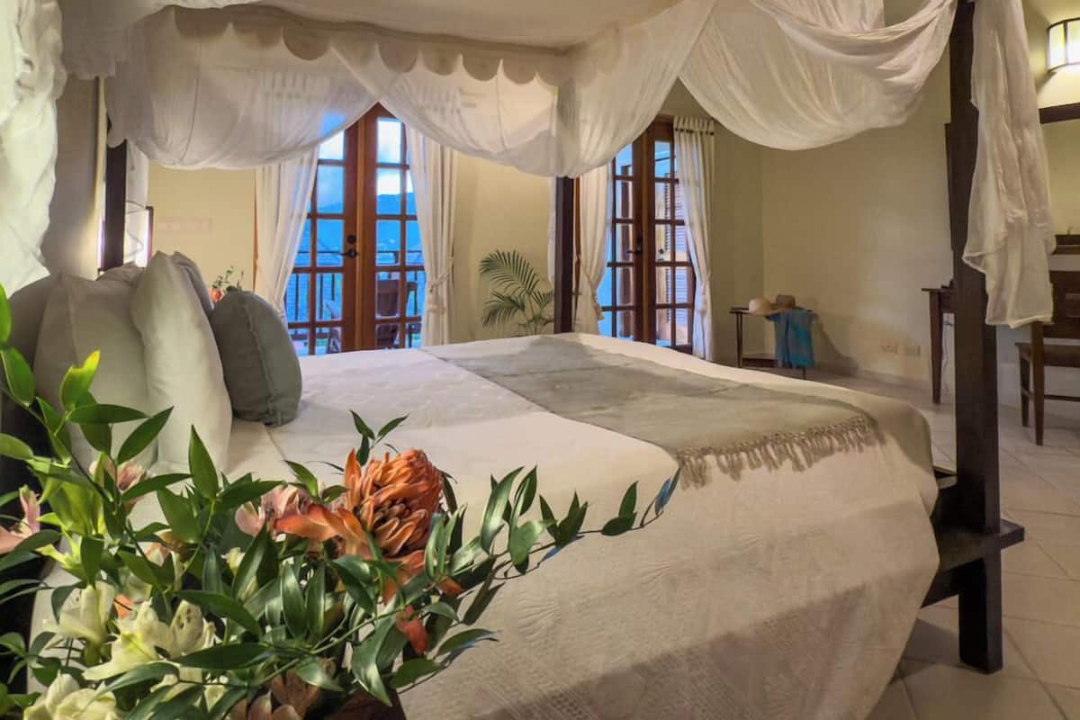 A bedroom with a canopy bed, large windows, and a view of the sea.
