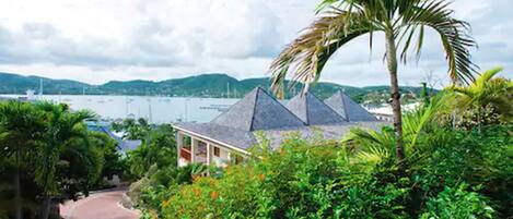 A hotel with a pyramid-shaped roof, surrounded by lush greenery and a view of the sea.