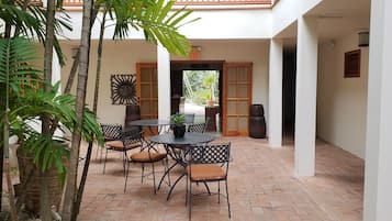 Een terras buiten met een ronde tafel en stoelen, omringd door potplanten en een houten deur.