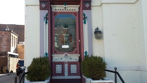 A building entrance with a decorative facade, steps leading up to it, and a small garden area with two bushes. - Inn Port Lodging (Dayton)