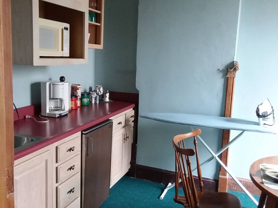 Una cocina funcional con armarios de madera, microondas, cafetera y comedor con una silla y mesa.