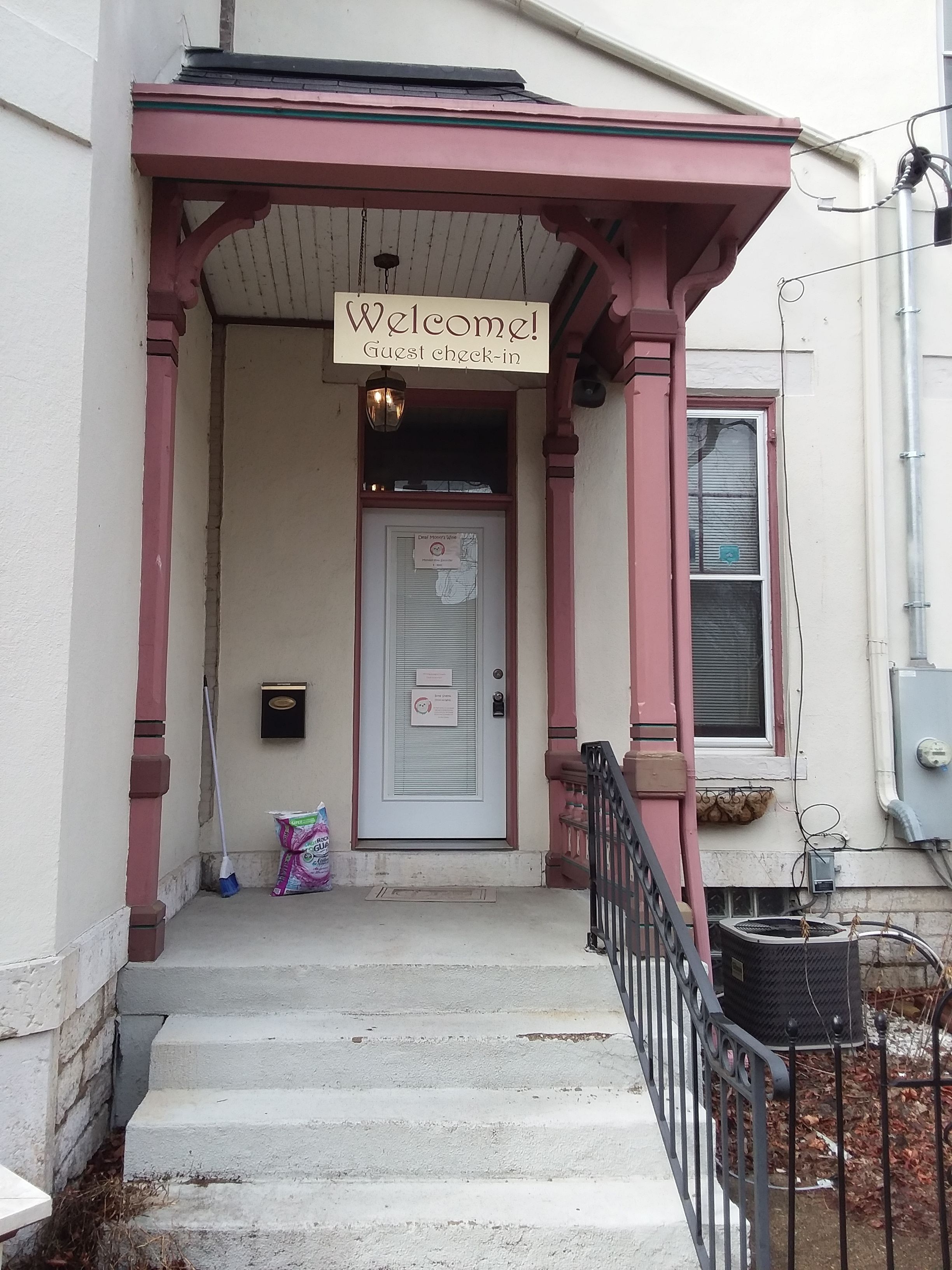A guest check-in area with a 'Welcome!' sign, a door with a notice, and a staircase leading to the entrance.