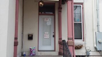 A guest check-in area with a 'Welcome!' sign, a door with a notice, and a staircase leading to the entrance.