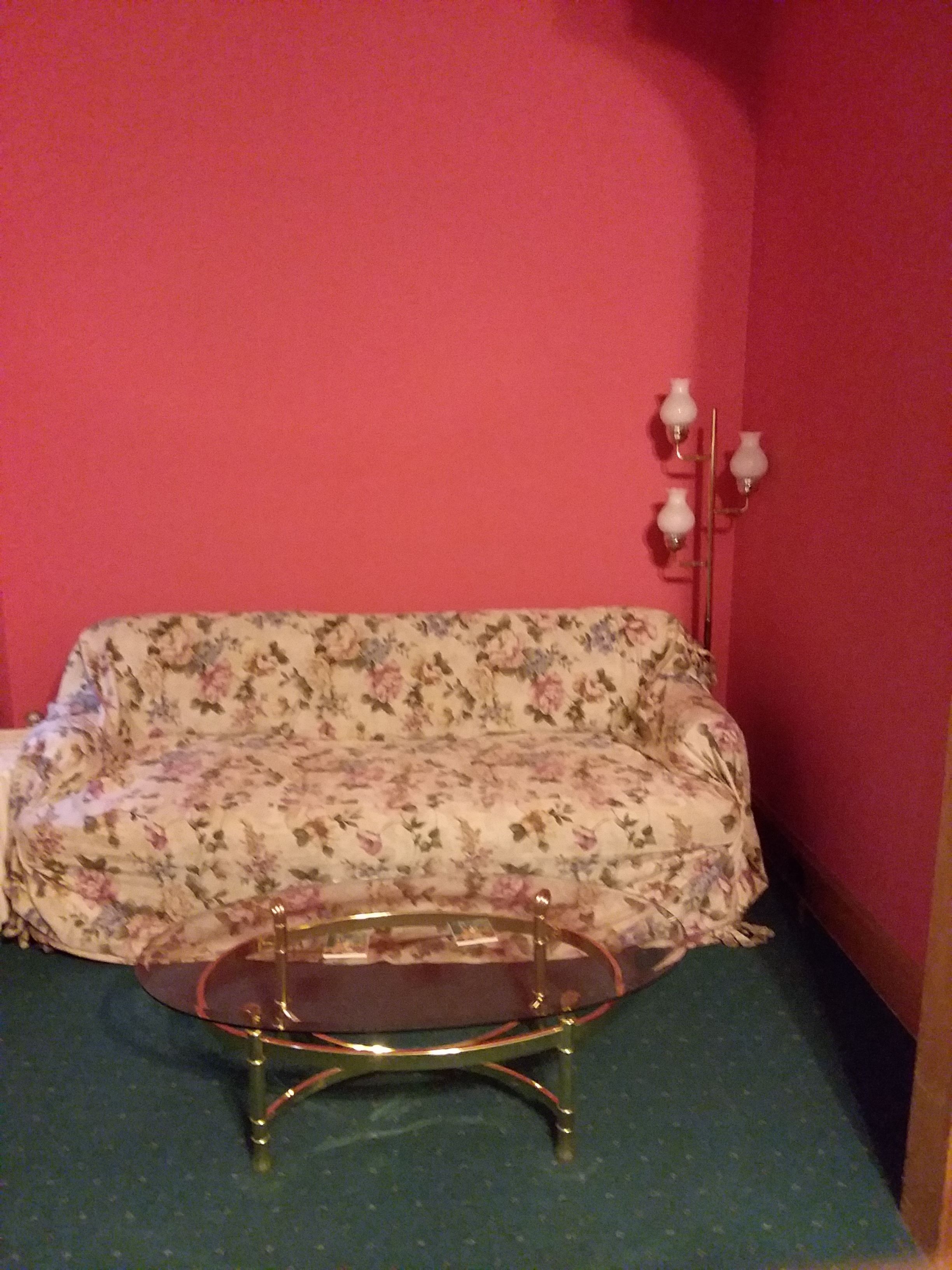 Una habitación con un sofá estampado con motivos florales, una mesa de centro de vidrio y una lámpara de pared.