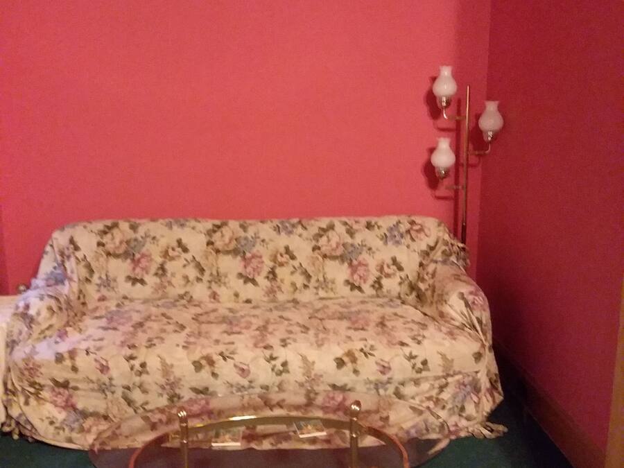 Una habitación con un sofá estampado con motivos florales, una mesa de centro de vidrio y una lámpara de pared.