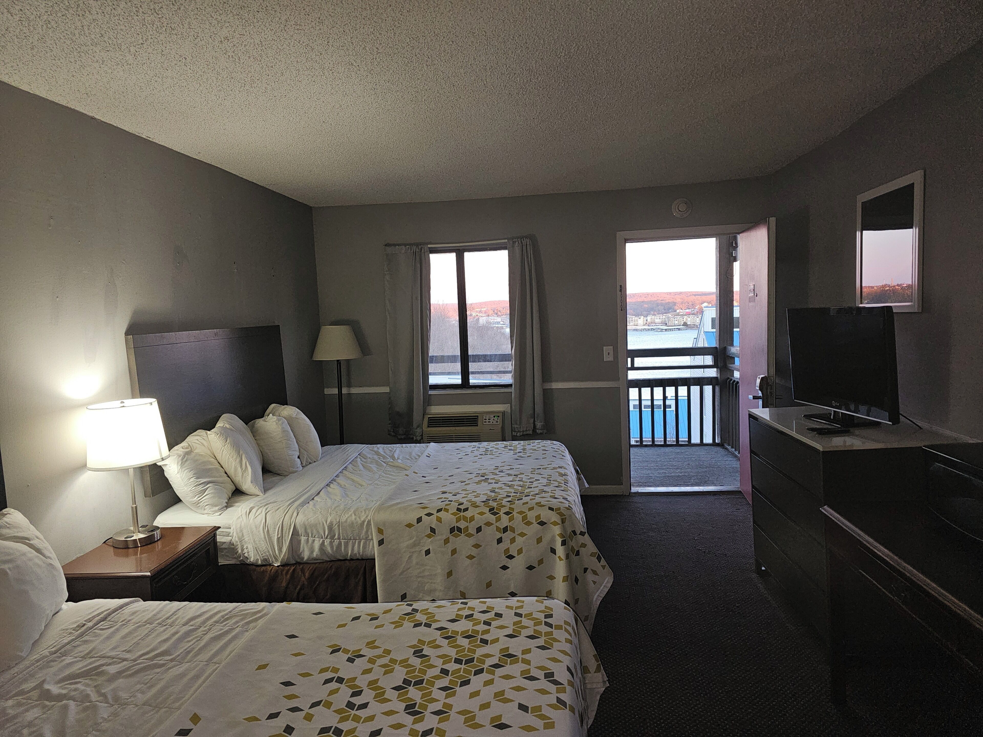 A hotel room with two beds, a TV, a lamp, a window with a view, and a balcony.
