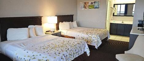 A hotel room with two beds, a desk, a chair, a nightstand with a lamp, and a bathroom visible through an open door.