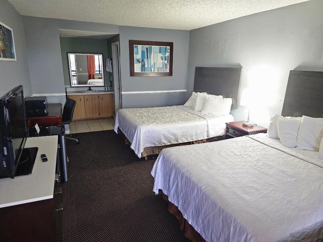 A hotel room with two beds, a desk, a chair, a mirror, and a bathroom visible through an open door.