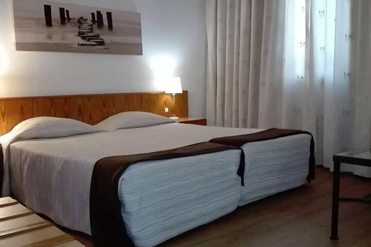 Habitación de hotel con una cama grande, cabecera de madera, una mesita de noche con lámpara y un cuadro en la pared.