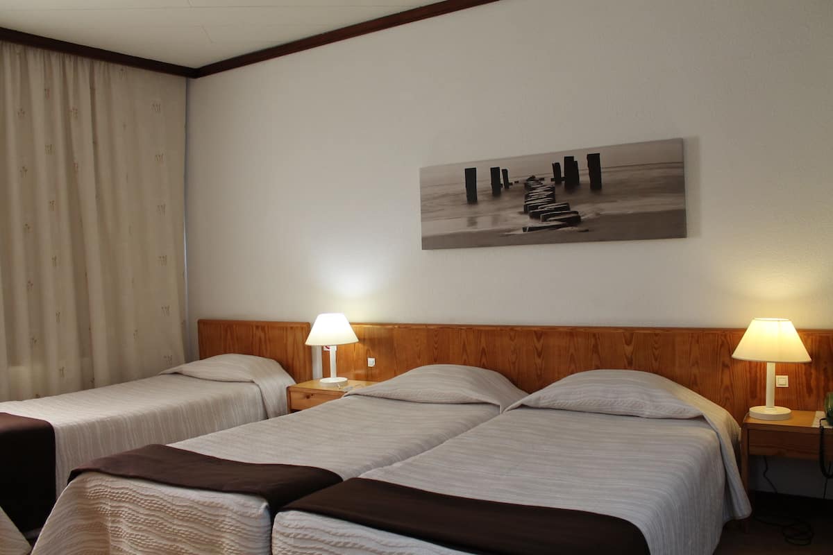 Habitación de hotel con dos camas individuales, cabeceros de madera, mesitas de noche con lámparas, un cuadro abstracto grande en la pared y una ventana con cortinas.