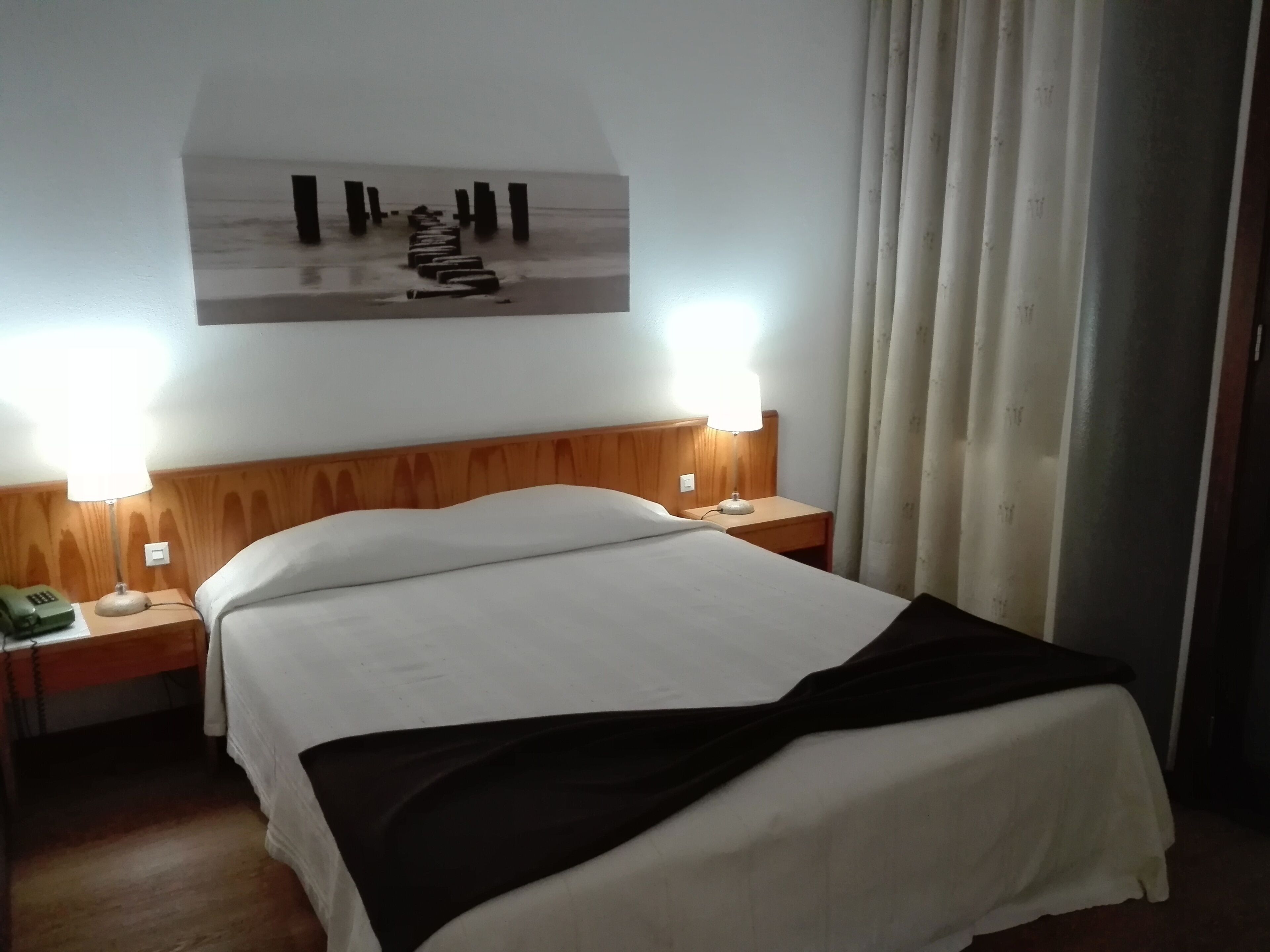 Une chambre d’hôtel avec un lit, deux lampes de chevet, un téléphone et un tableau au mur.
