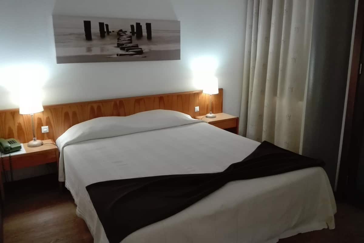 Una habitación de hotel con cama, dos lámparas de noche, un teléfono y un cuadro en la pared.