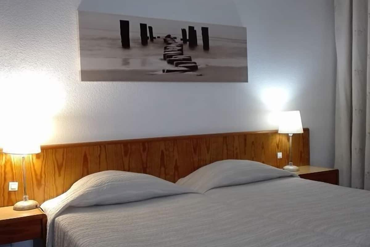 Habitación de hotel con cama, cabecero de madera, dos lámparas de noche y una obra de arte en la pared que muestra un muelle.