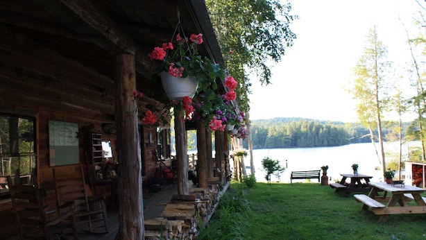 A rustic cabin with a porch, wooden furniture, and hanging flower baskets. - Kiwassa Lake Bed & Breakfast (Saranac Lake)