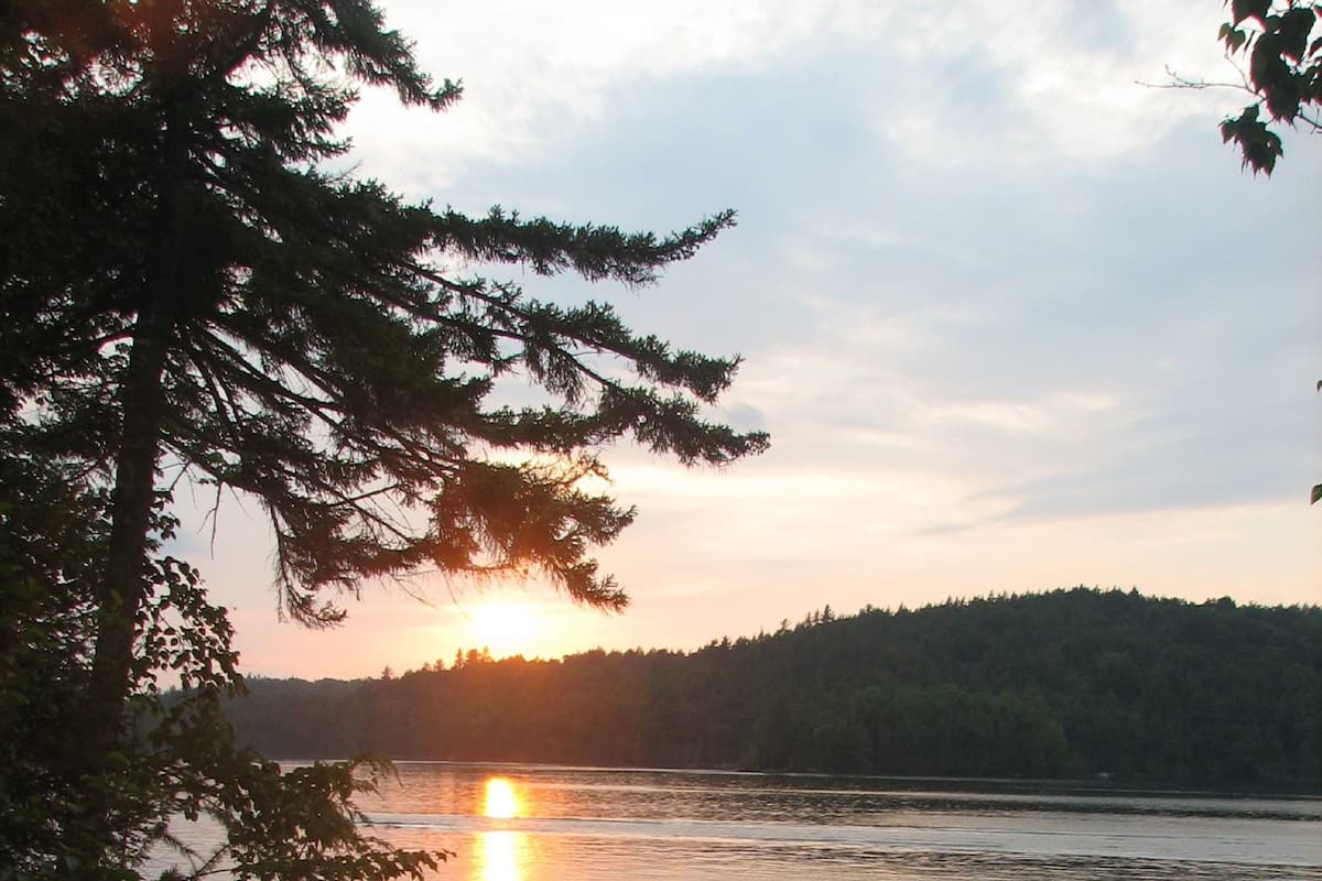 Un coucher de soleil sur un lac paisible, avec un quai et des arbres au premier plan.
