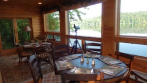 A wooden cabin with a round dining table, chairs, and a telescope. - Kiwassa Lake Bed & Breakfast (Saranac Lake)