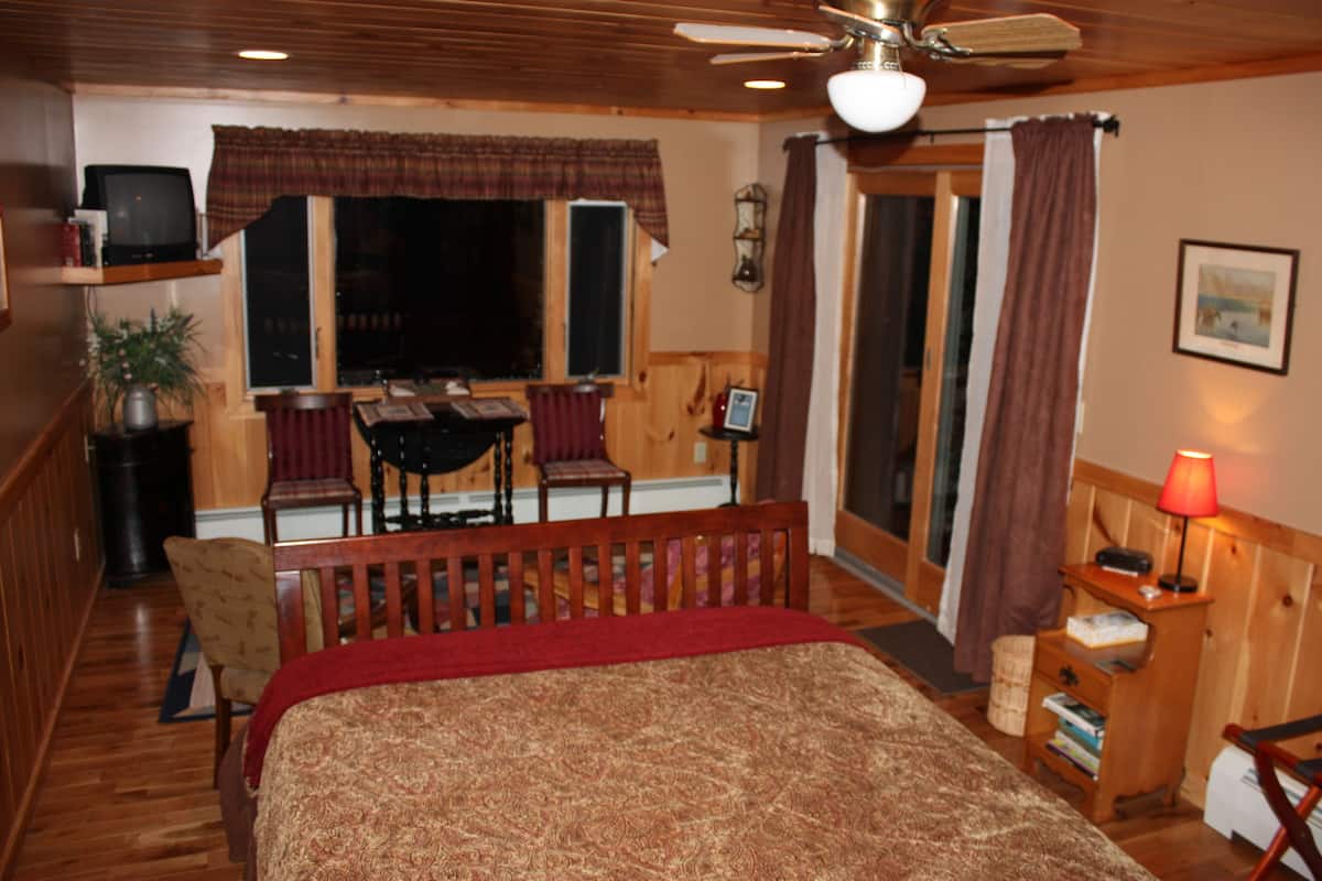 Une chambre à coucher comprenant un lit, un bureau, une chaise, un téléviseur et une fenêtre avec des rideaux.