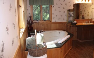 Un baño con una bañera de madera, un lavabo, un espejo y una ventana con vistas a árboles.