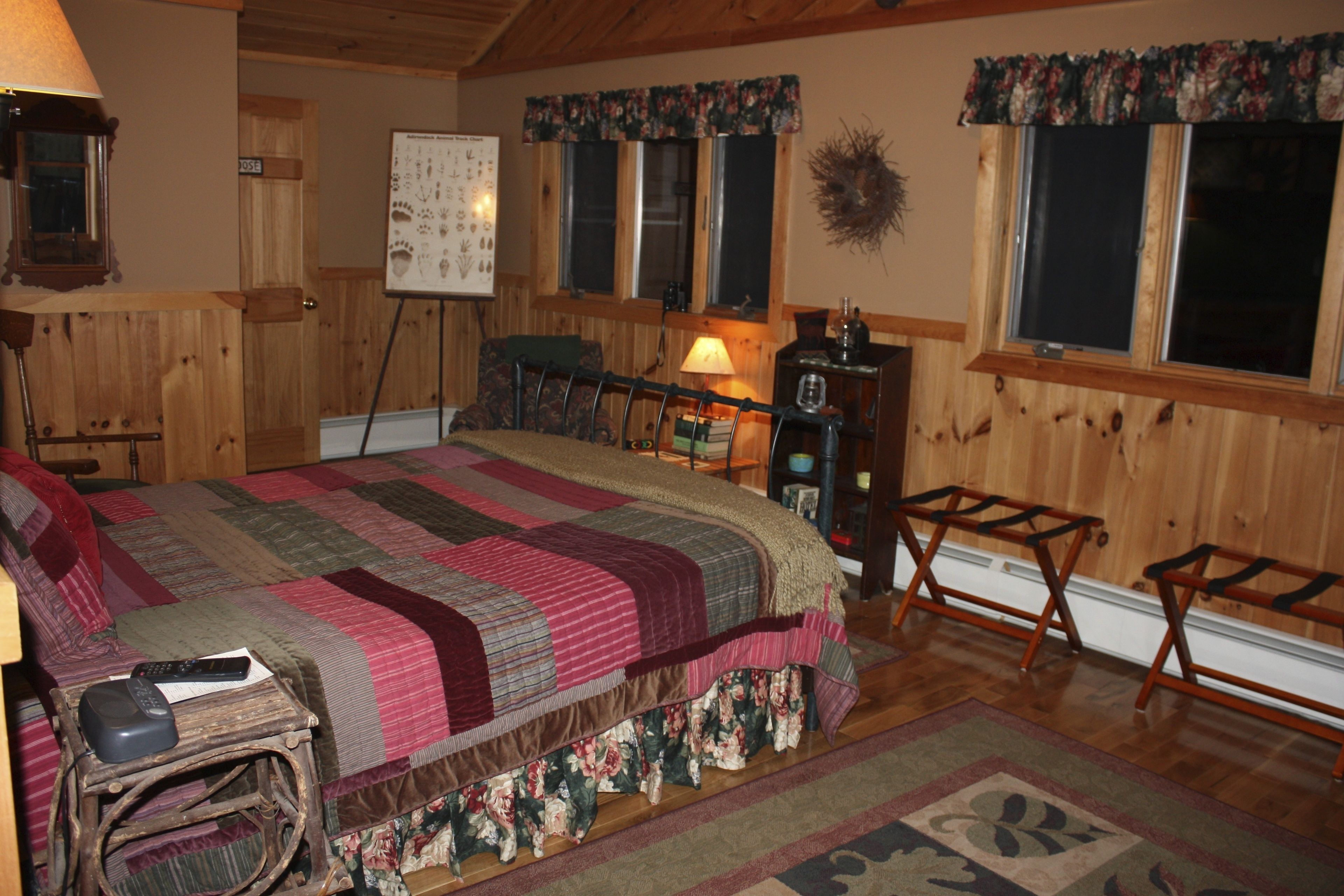 A cozy room with a large bed, a wooden floor, a desk with a lamp, and a window with a floral curtain.