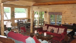 A log cabin interior with a living room, dining area, and large windows offering views of the outdoors. - Kiwassa Lake Bed & Breakfast (Saranac Lake)