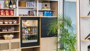 A compact kitchen with a refrigerator, shelves with food items, and a potted plant.