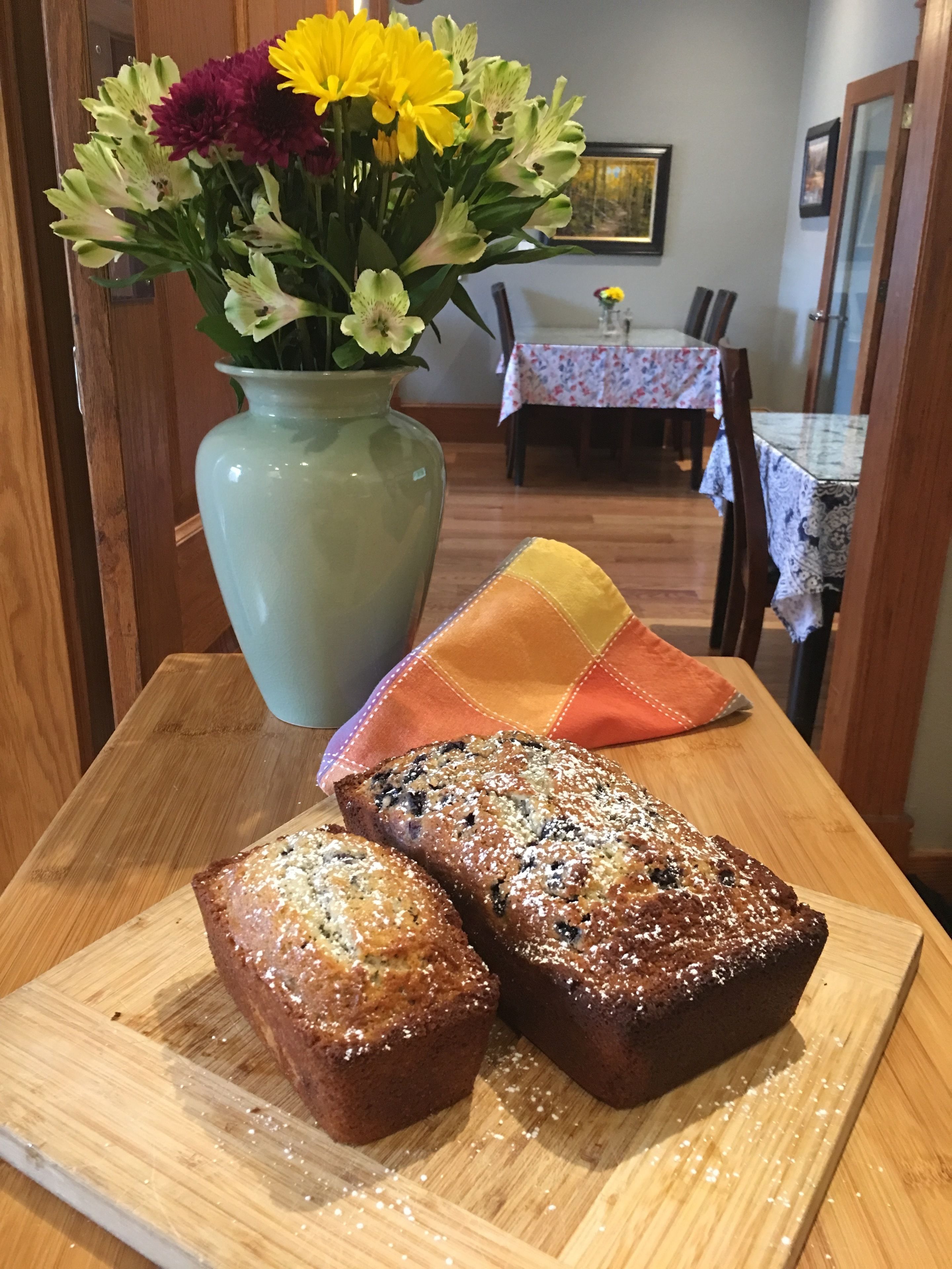 A wooden table with two loaves of bread and a vase of flowers.