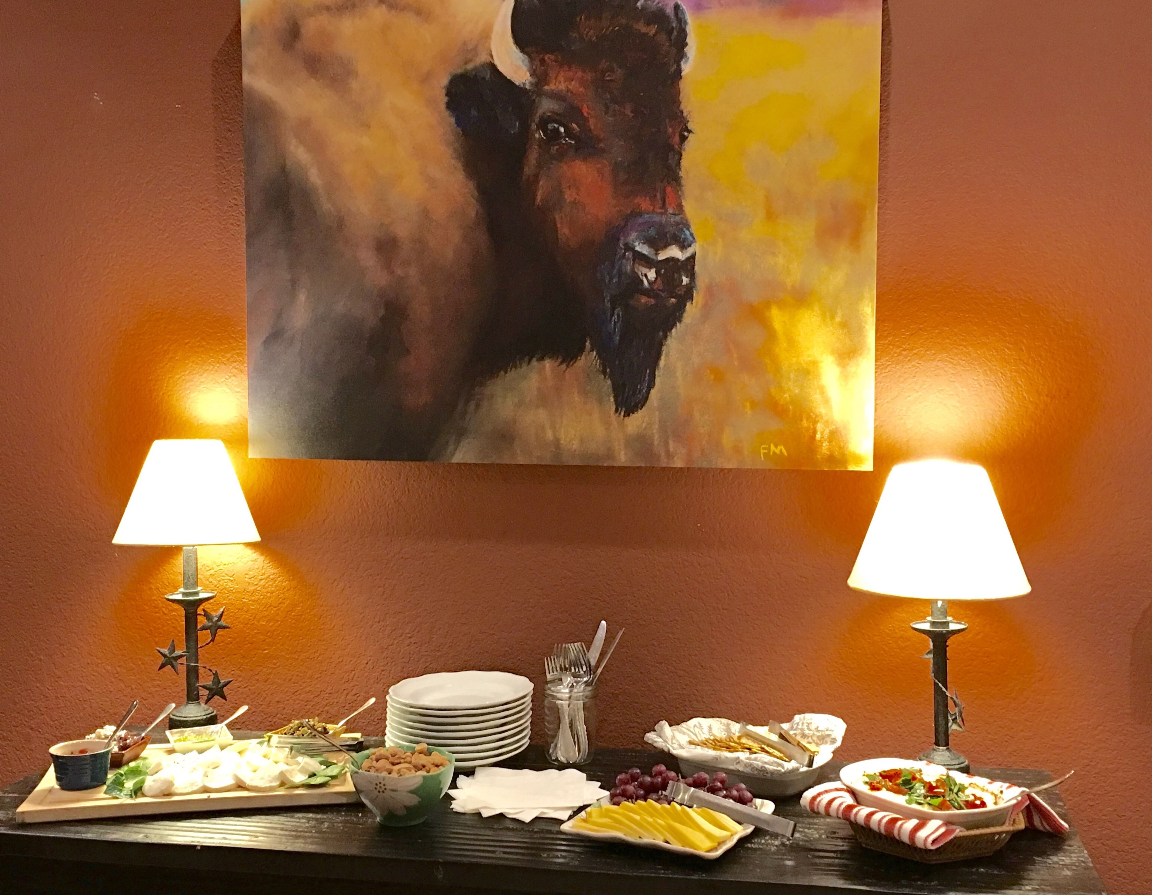 A buffet table with various dishes, two wall-mounted lamps, and a painting of a buffalo.