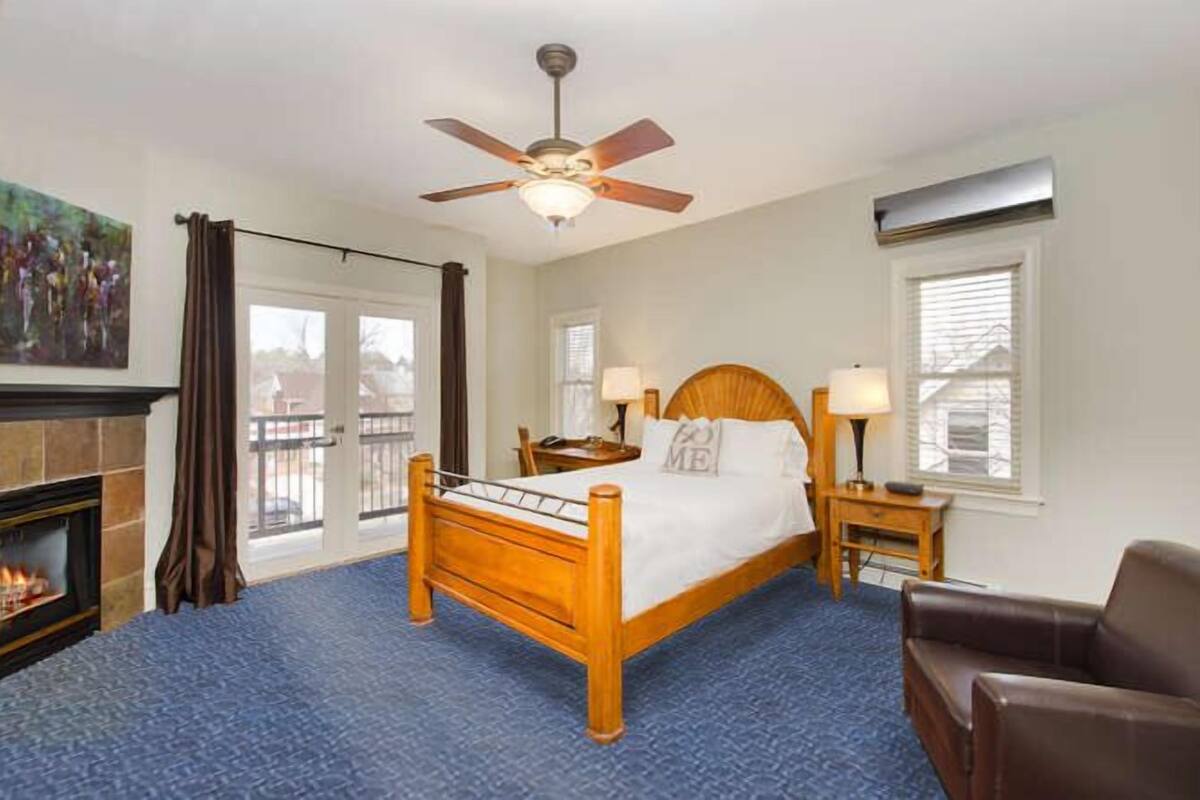 A hotel room with a wooden bed, a ceiling fan, a fireplace, and a view of the outside.