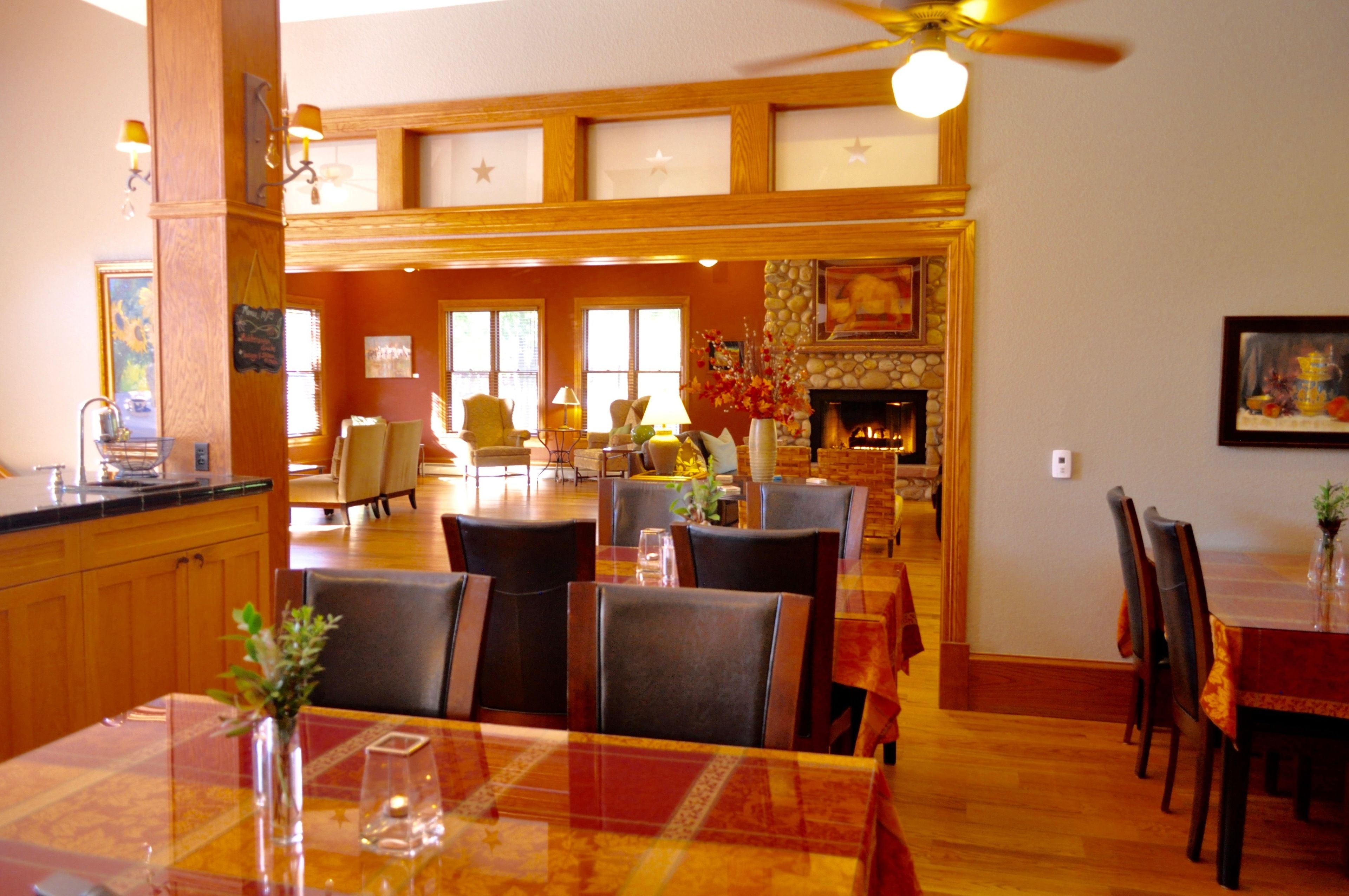 A dining area with wooden tables and chairs, a fireplace, and a view of the kitchen area.
