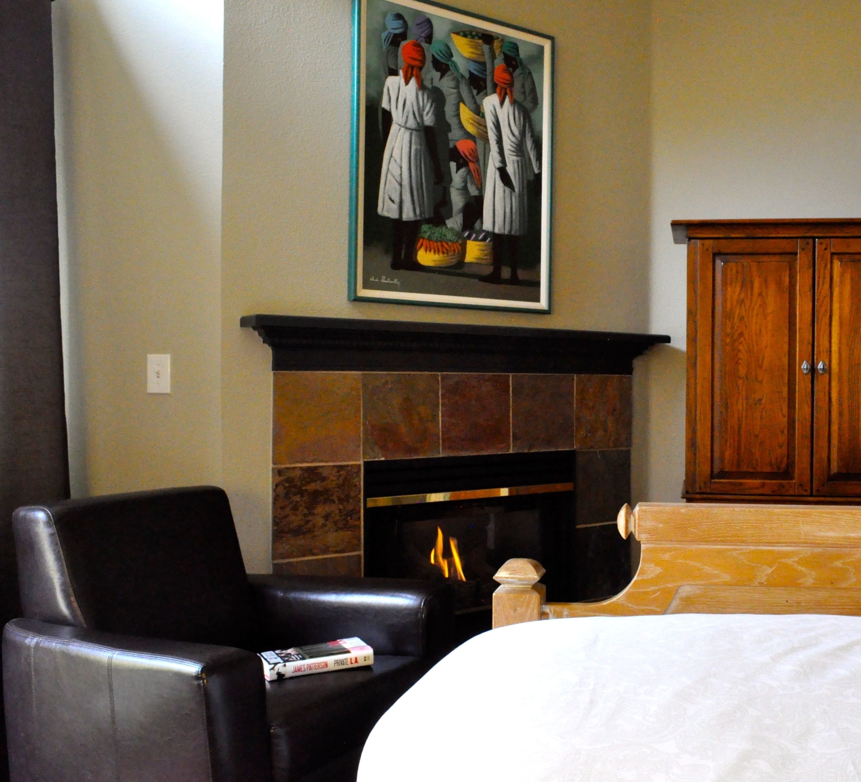 Habitación de hotel con chimenea, un sillón de cuero, una cama y un cuadro sobre la chimenea.