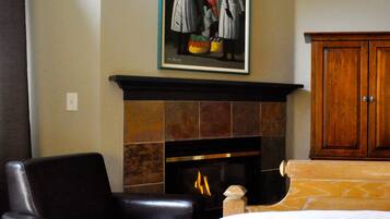 Habitación de hotel con chimenea, un sillón de cuero, una cama y un cuadro sobre la chimenea.