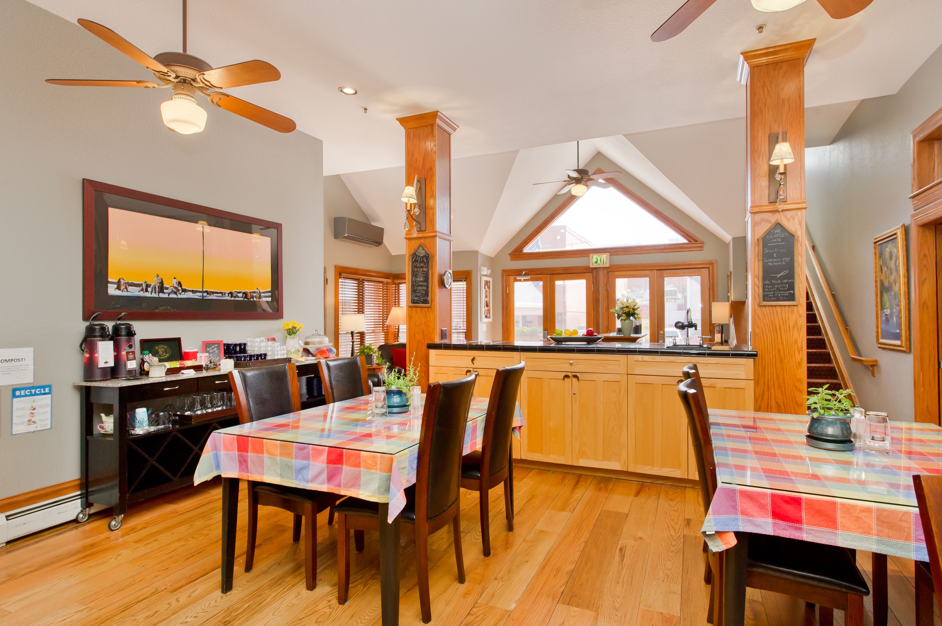 A dining area with a table set for two, wooden cabinets, a kitchen counter, and a ceiling fan.