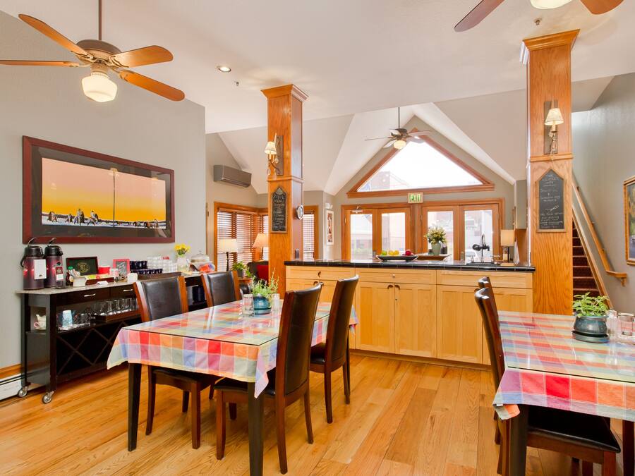A dining area with a table set for two, wooden cabinets, a kitchen counter, and a ceiling fan.