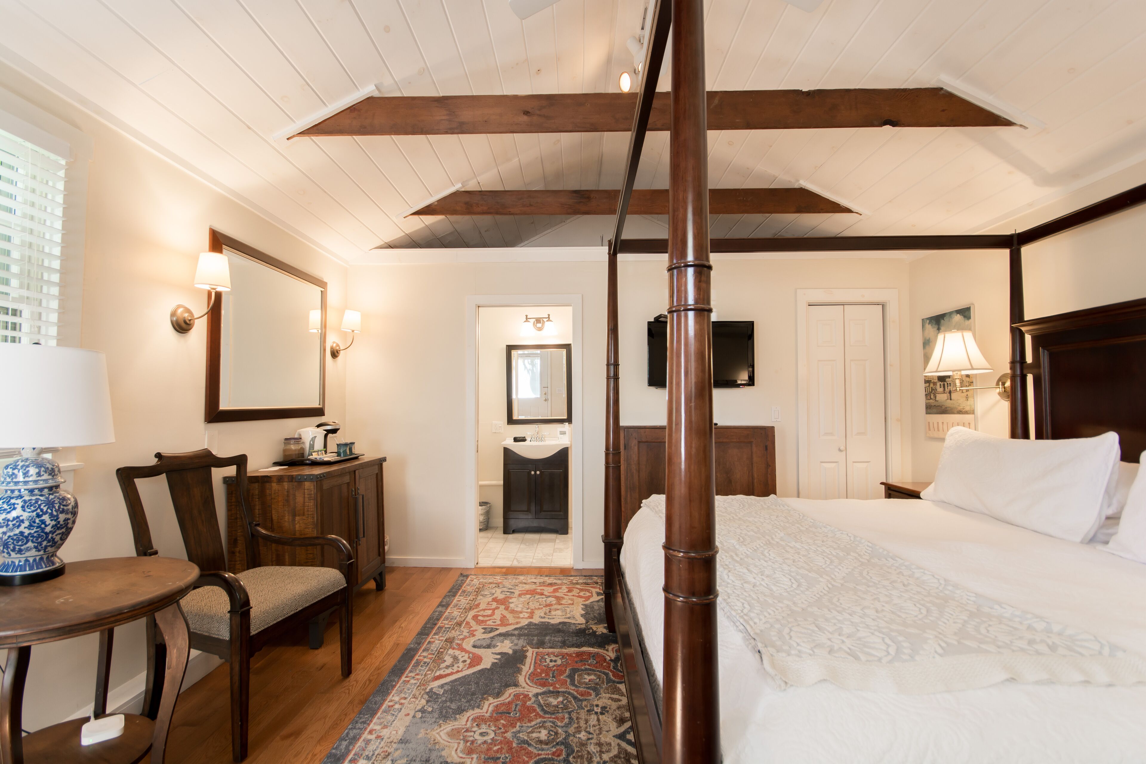 A bedroom with a four-poster bed, wooden furniture, a large mirror, and a view of the bathroom.