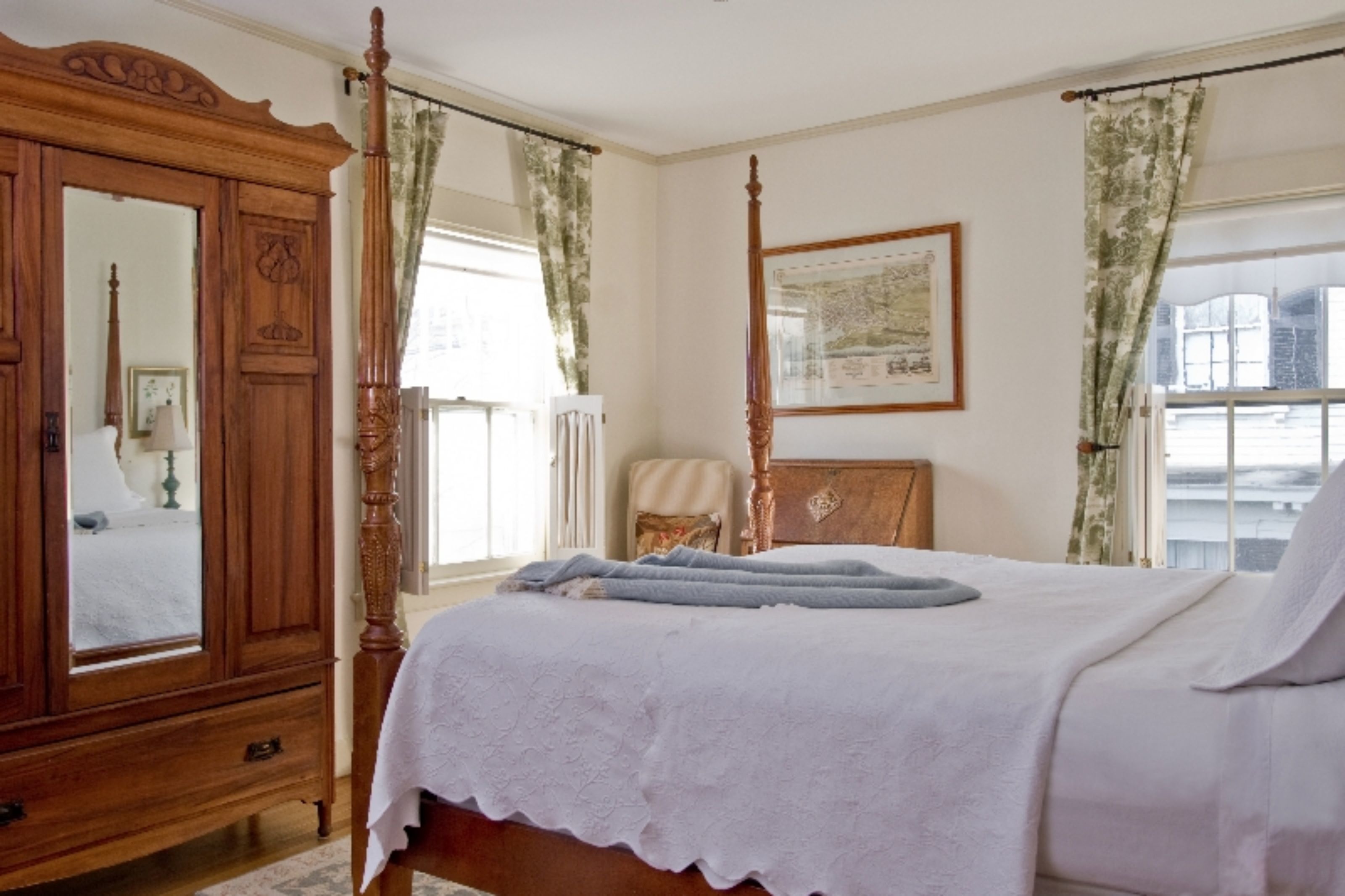 A bedroom with a four-poster bed, a wooden wardrobe, and a large mirror.