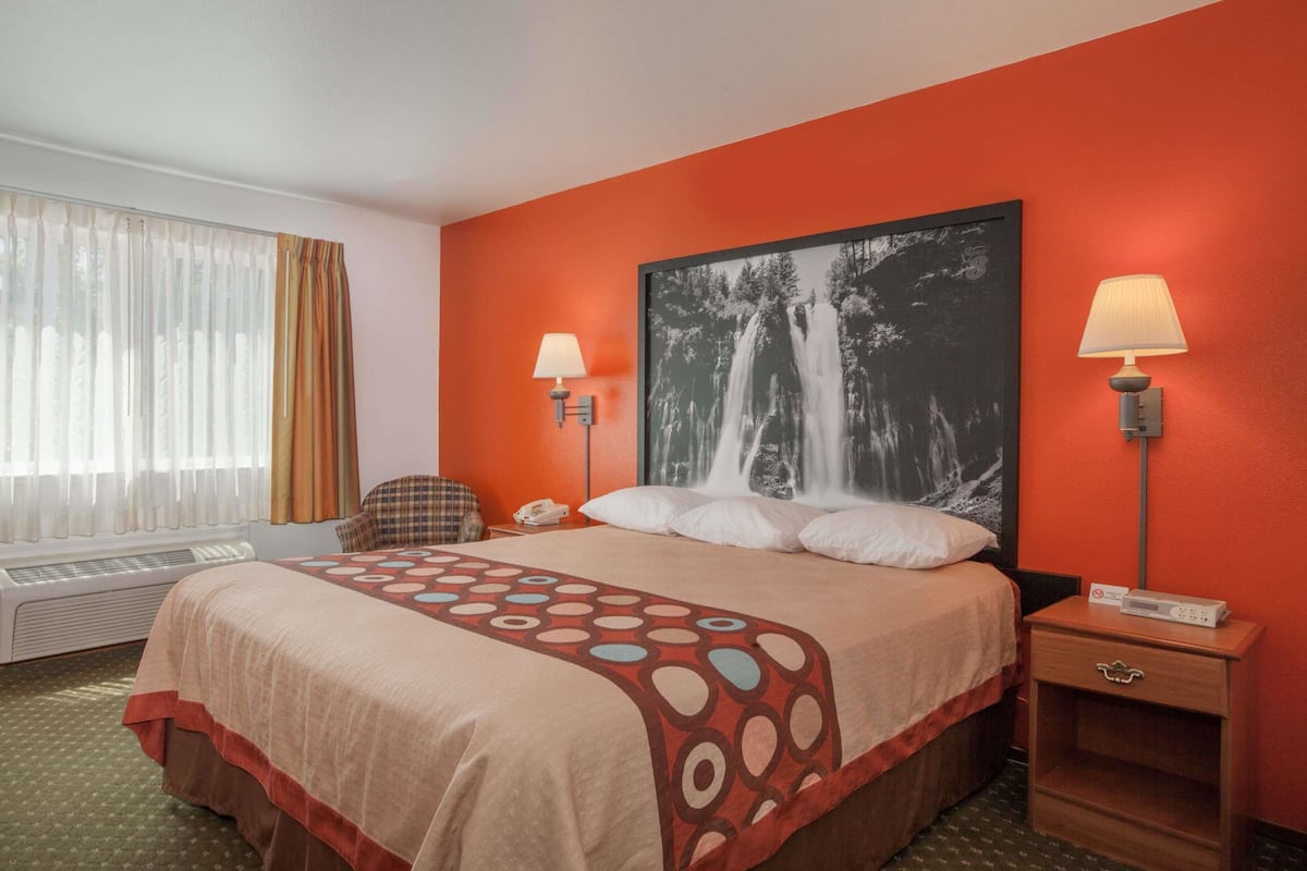 Camera d'albergo con un letto grande, due abat-jour, un termosifone, una sedia e un quadro incorniciato di grandi dimensioni appeso al muro.