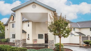 A two-story building with a beige facade, a stone pillar, and a small tree in the foreground. - Super 8 by Wyndham Cloverdale Wine Country (Cloverdale)