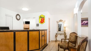 A hotel lobby with a reception desk, a clock, a Super 8 sign, a mirror, and a chair. - Super 8 by Wyndham Cloverdale Wine Country (Cloverdale)