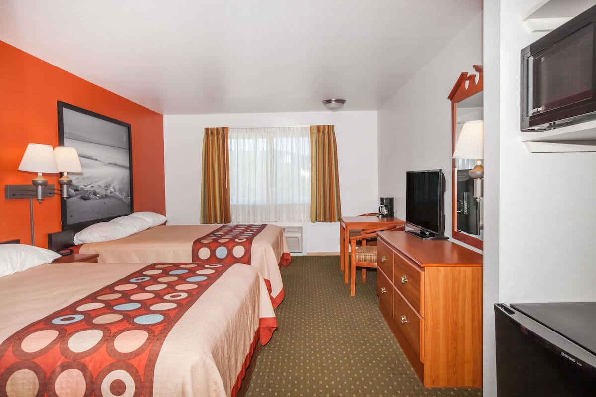 Camera d'albergo con due letti, una scrivania, una TV e un'ampia finestra con tende.