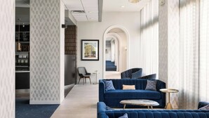 A modern hotel lobby with a blue sofa set, a round coffee table, and a bookshelf.