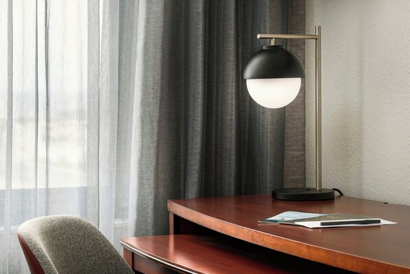 A modern room with a wooden desk, a chair, a black floor lamp, and a window with sheer curtains.