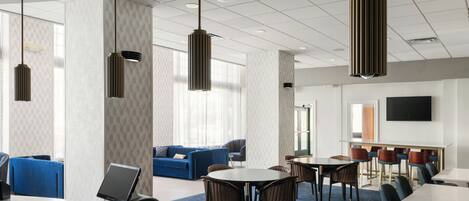 A modern hotel lobby with a reception desk, seating area, and a large TV screen.