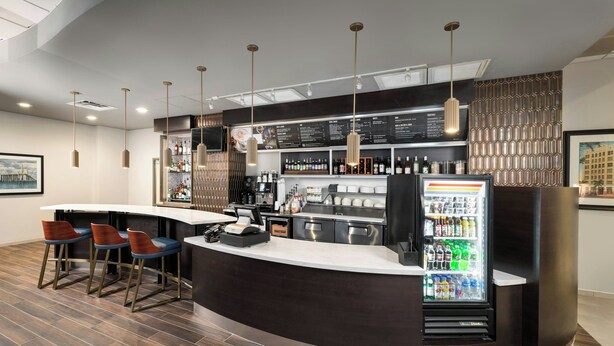 A modern bar area with a curved counter, bar stools, a refrigerator stocked with beverages, and a menu board.