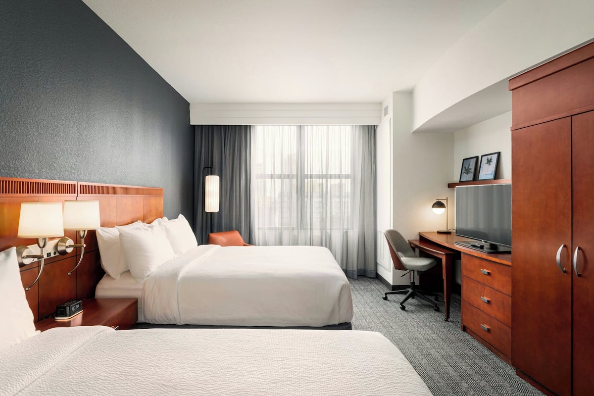 A hotel room with two beds, a desk, a TV, and a wardrobe.