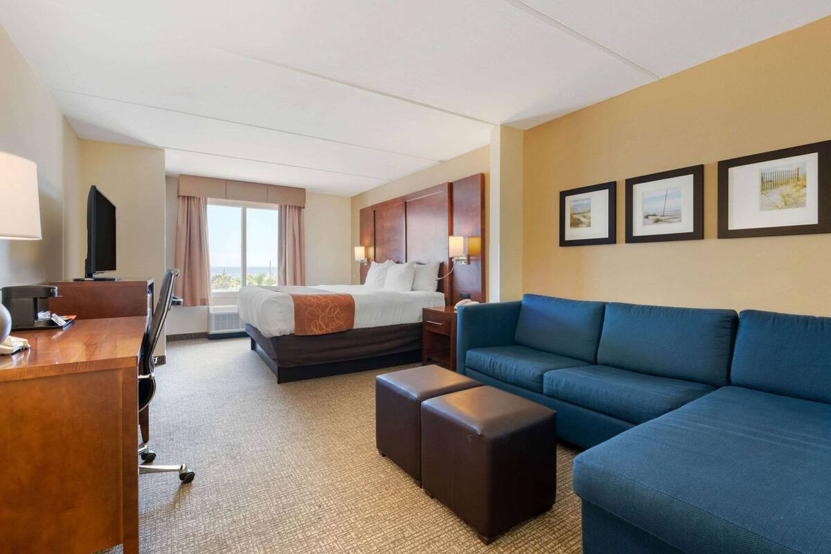A hotel room with a bed, a blue sofa, a desk with a lamp, and a TV.
