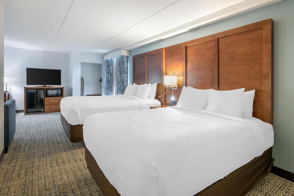 A hotel room with two beds, a TV, a minibar, and a marble wall.