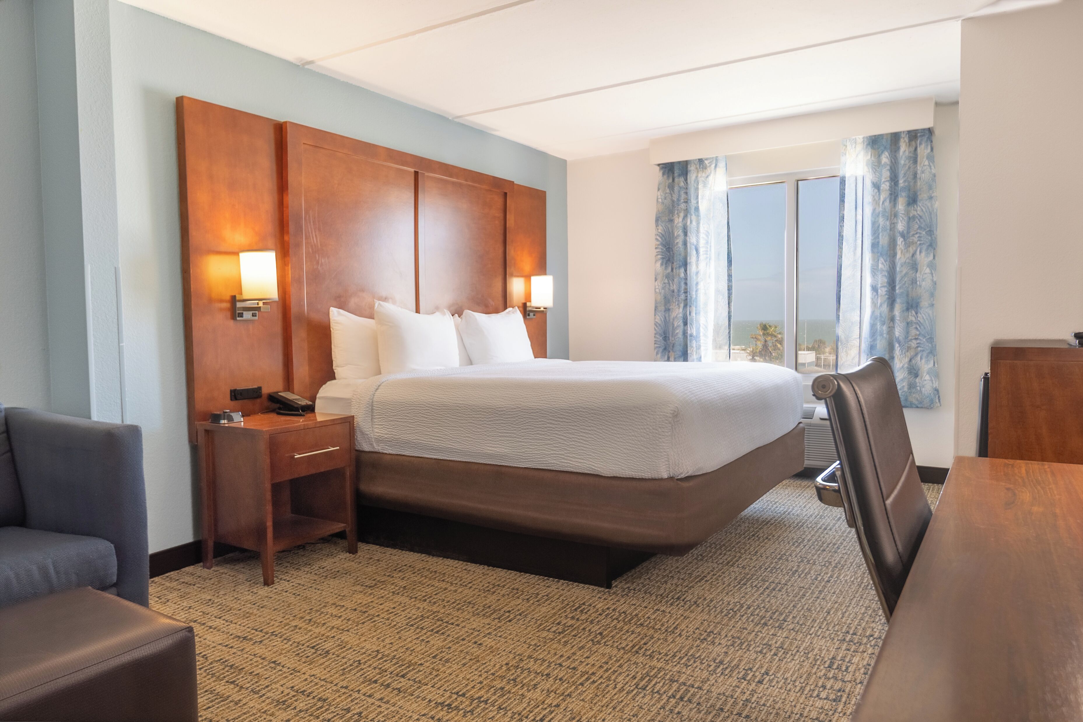 Een hotelkamer met een groot bed, nachtkastjes, een bureau, een stoel en uitzicht op de omgeving.