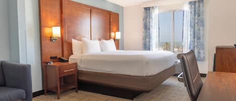 A hotel room with a large bed, bedside tables, a desk, a chair, and a view of the outdoors.