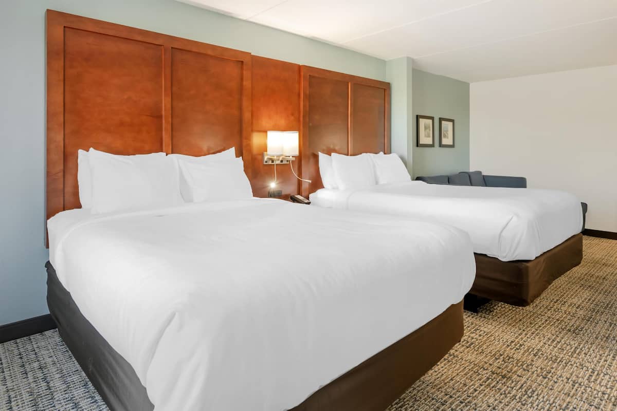 A hotel room with two beds, a wooden headboard, a nightstand with a lamp, and a carpeted floor.